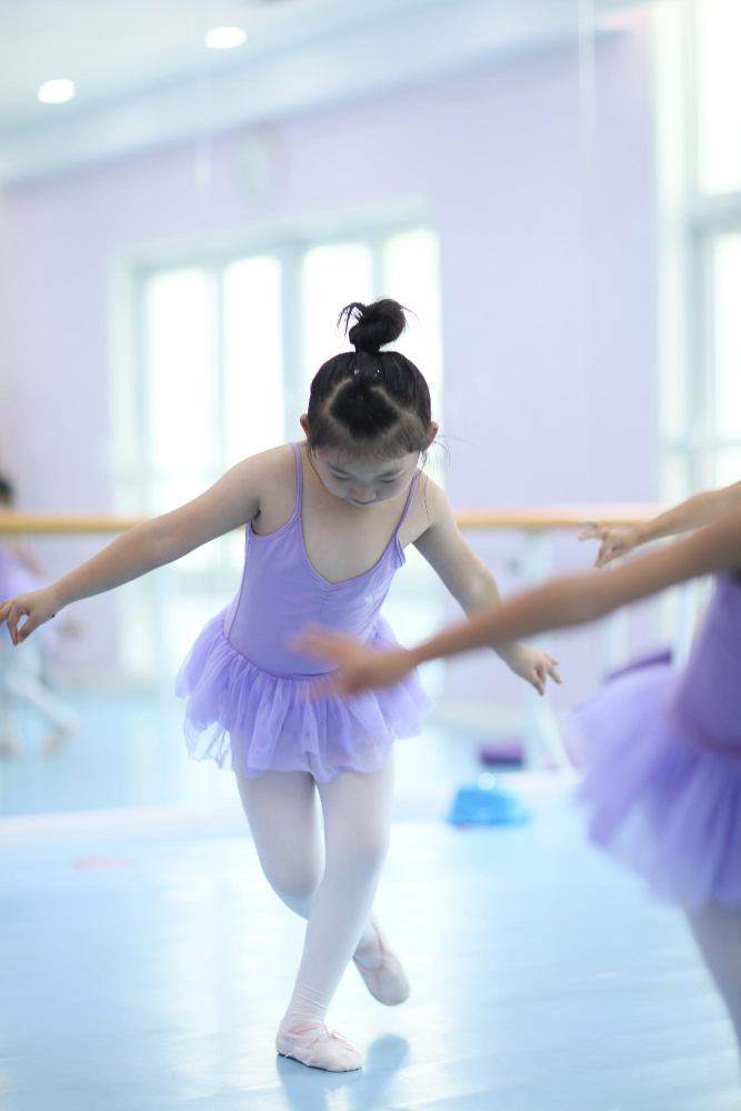 young girl in purple tutu leotard practicing during ballerina class